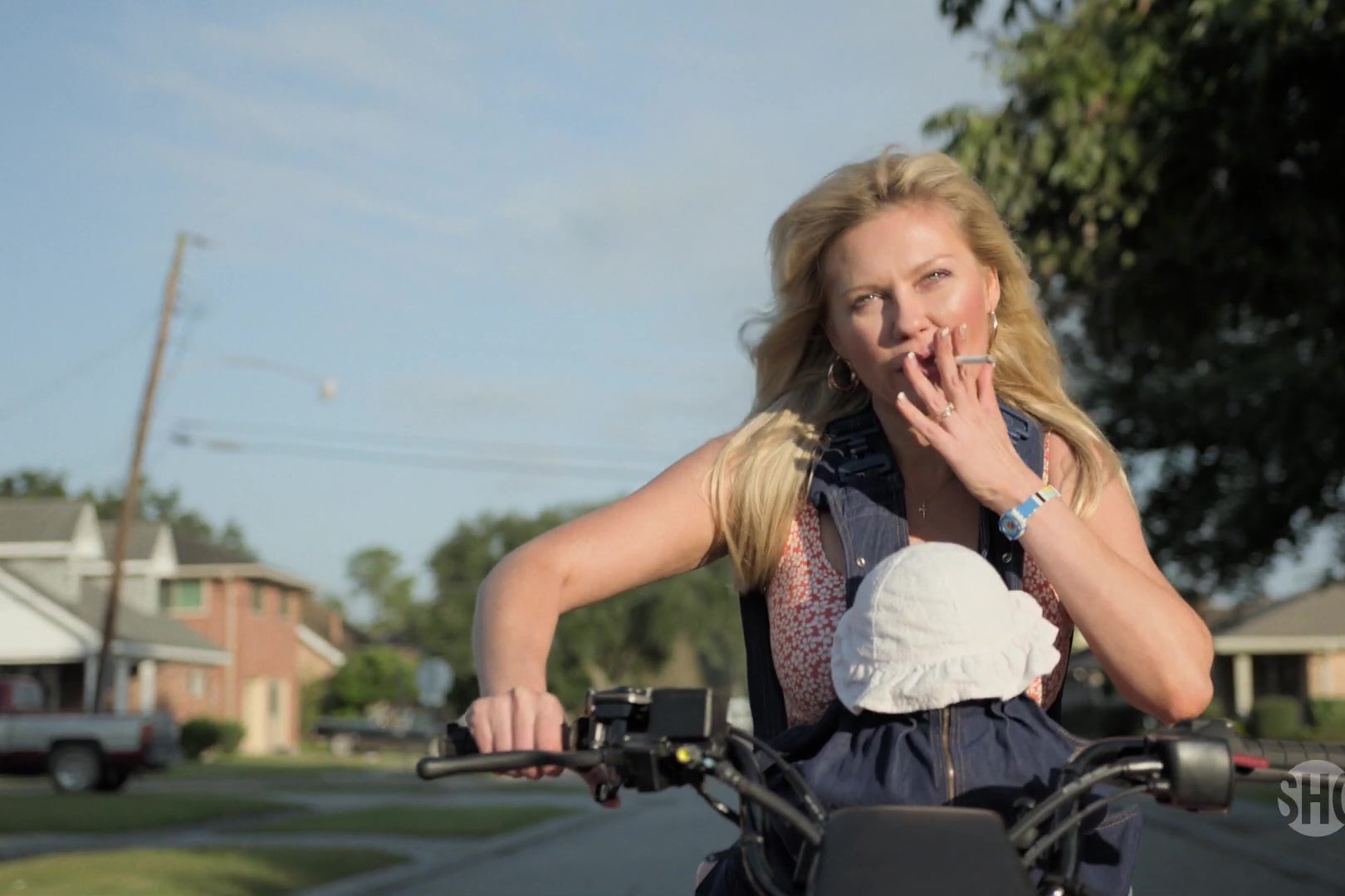 Kirsten Dunst riding a motorbike with a baby strapped to her chest, smoking a cigarette.
