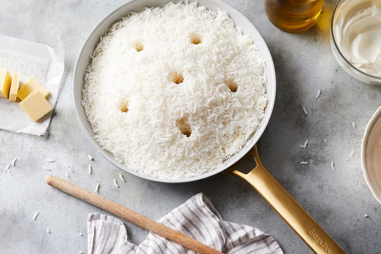 White rice in a pan on a grey marble countertop. Rice has six evenly-spaced holes made in it.