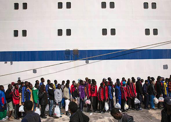 Migrant men wait in line to board a ship bound for Sicily.
