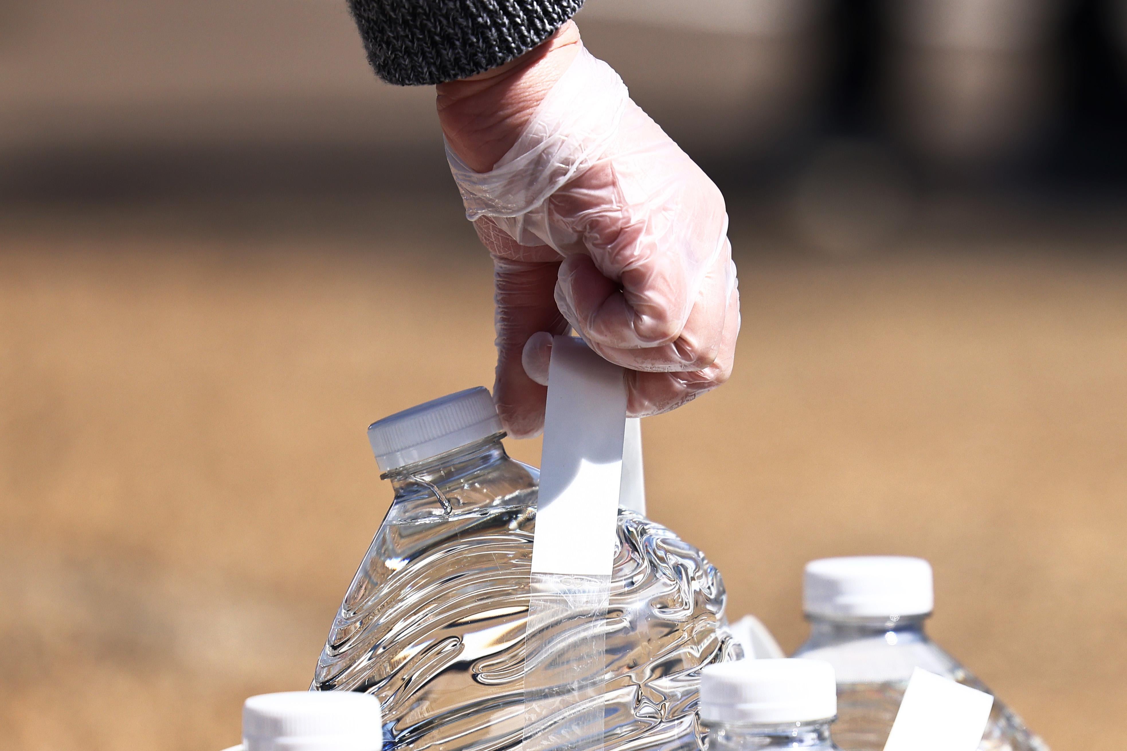 A gloved hand holds a gallon of water.