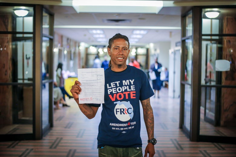 Michael Monfluery, wearing a shirt that says, "Let my people vote," holds up a piece of paper.