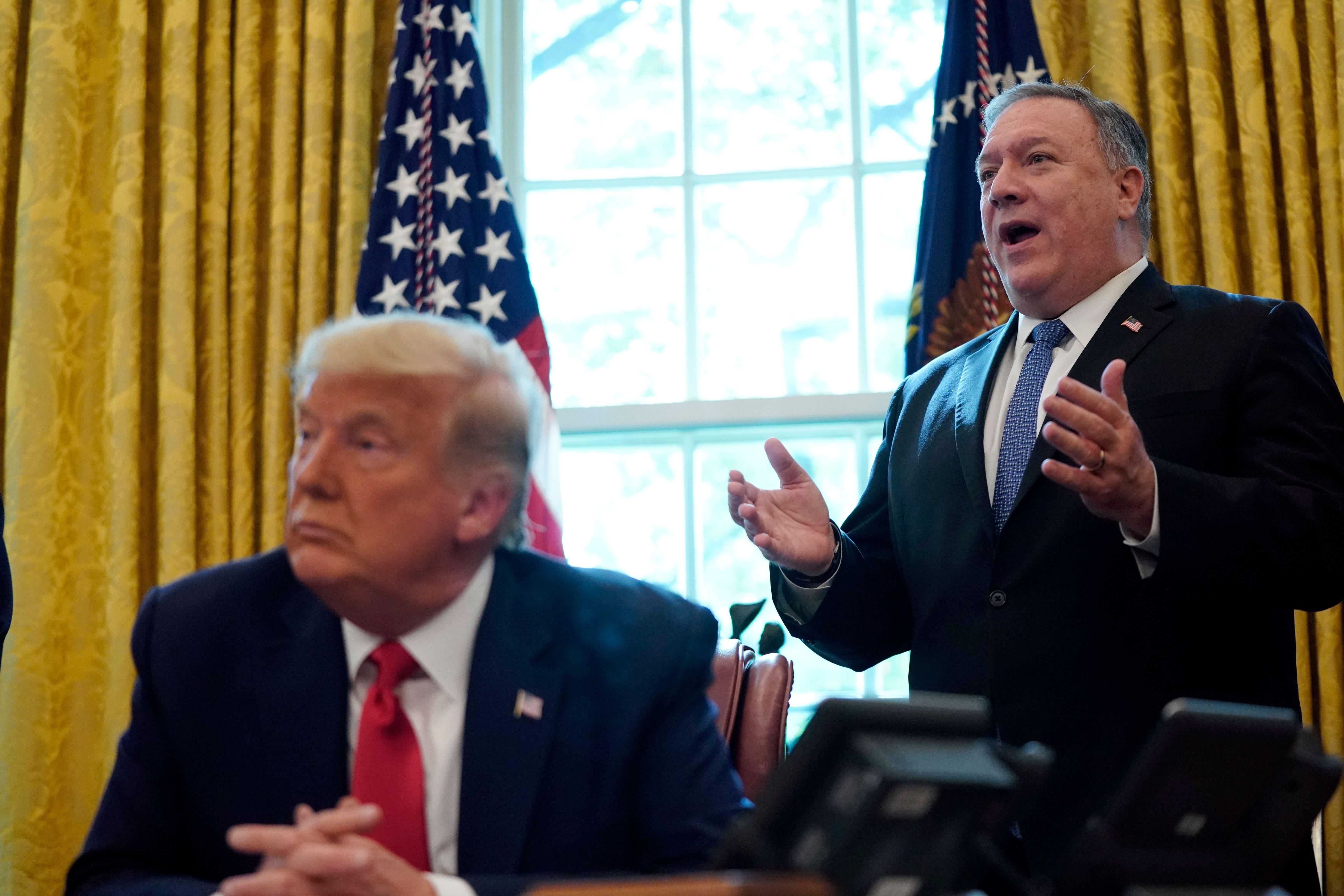 Mike Pompeo stands behind President Trump who's seated in the Oval Office.