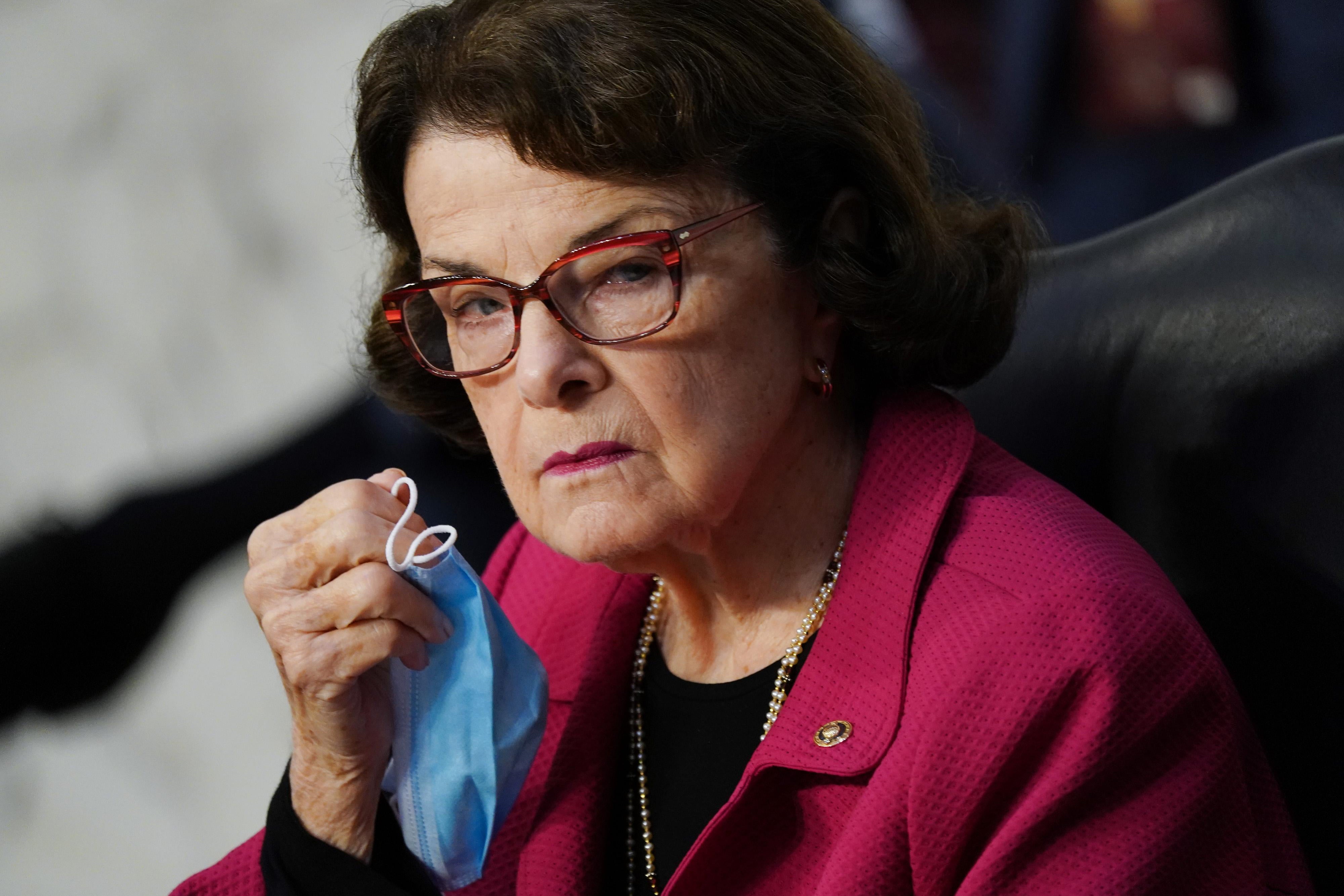 Dianne Feinstein holds a face mask and looks angrily to the side.