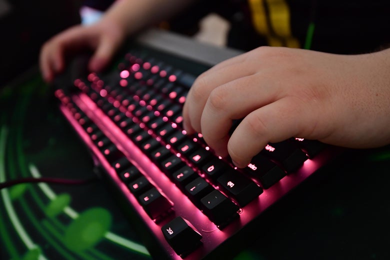 Two hands hover over a keyboard with pink backlighting.
