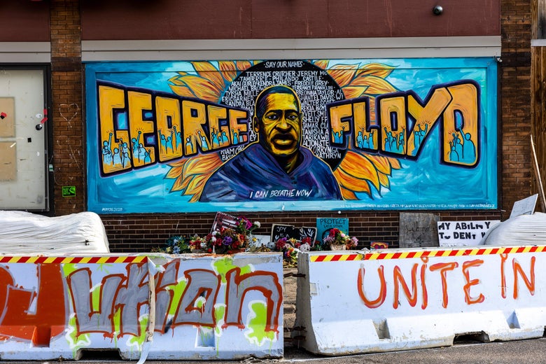 Barricades with graffiti are seen in front of a mural depicting George Floyd's face and name.