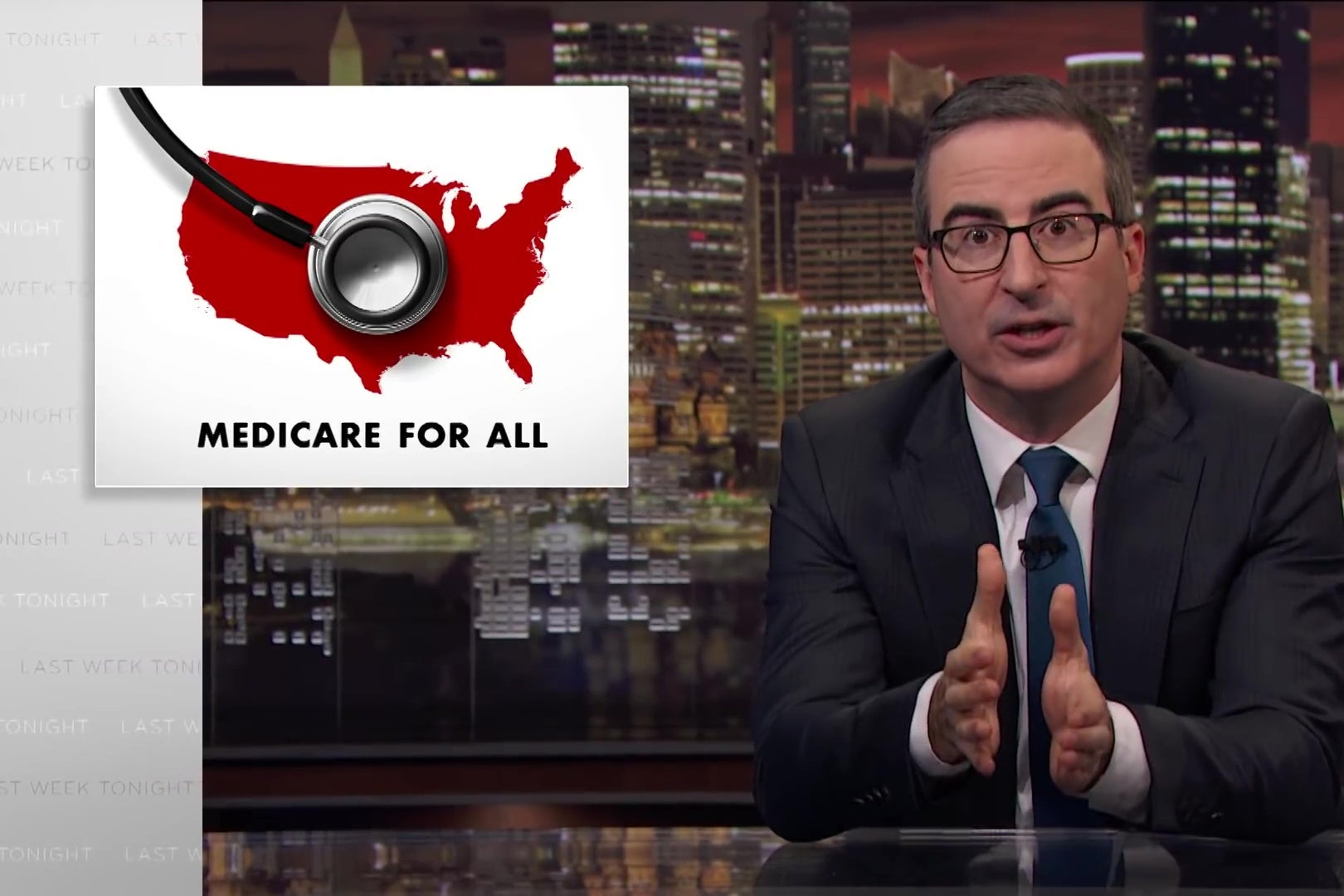 John Oliver sits at an anchorperson's desk, in front of an image reading "Medicare For All."