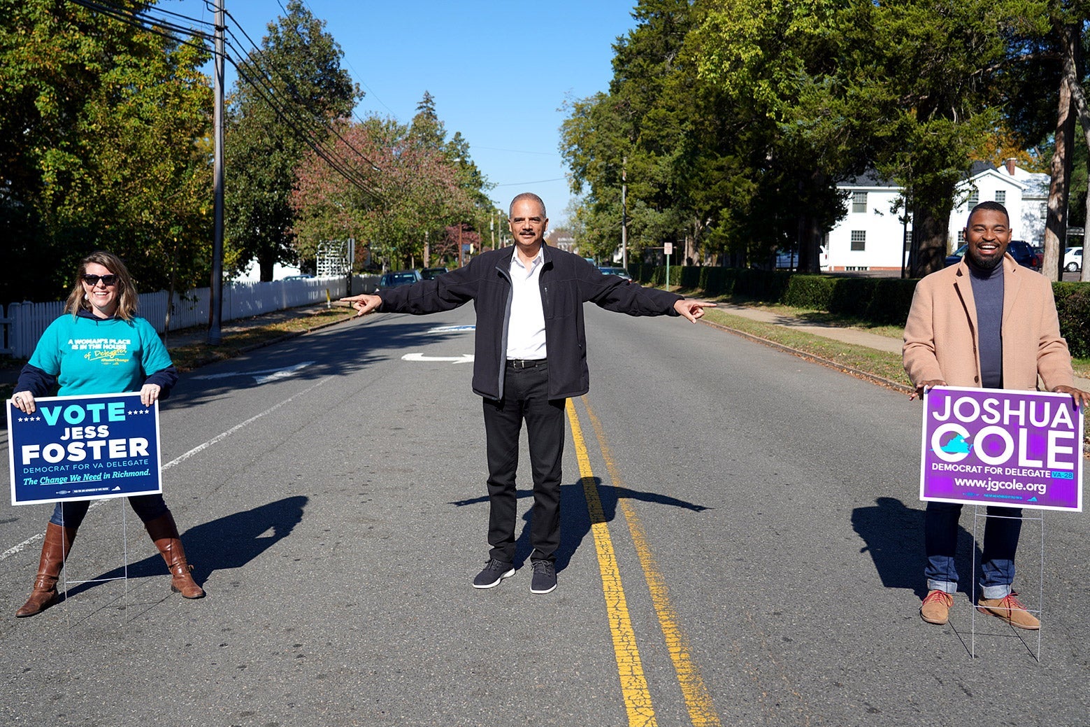 Eric Holder stands in the middle of the road and points at Jess Foster and Joshua Cole, who hold campaign yard signs.