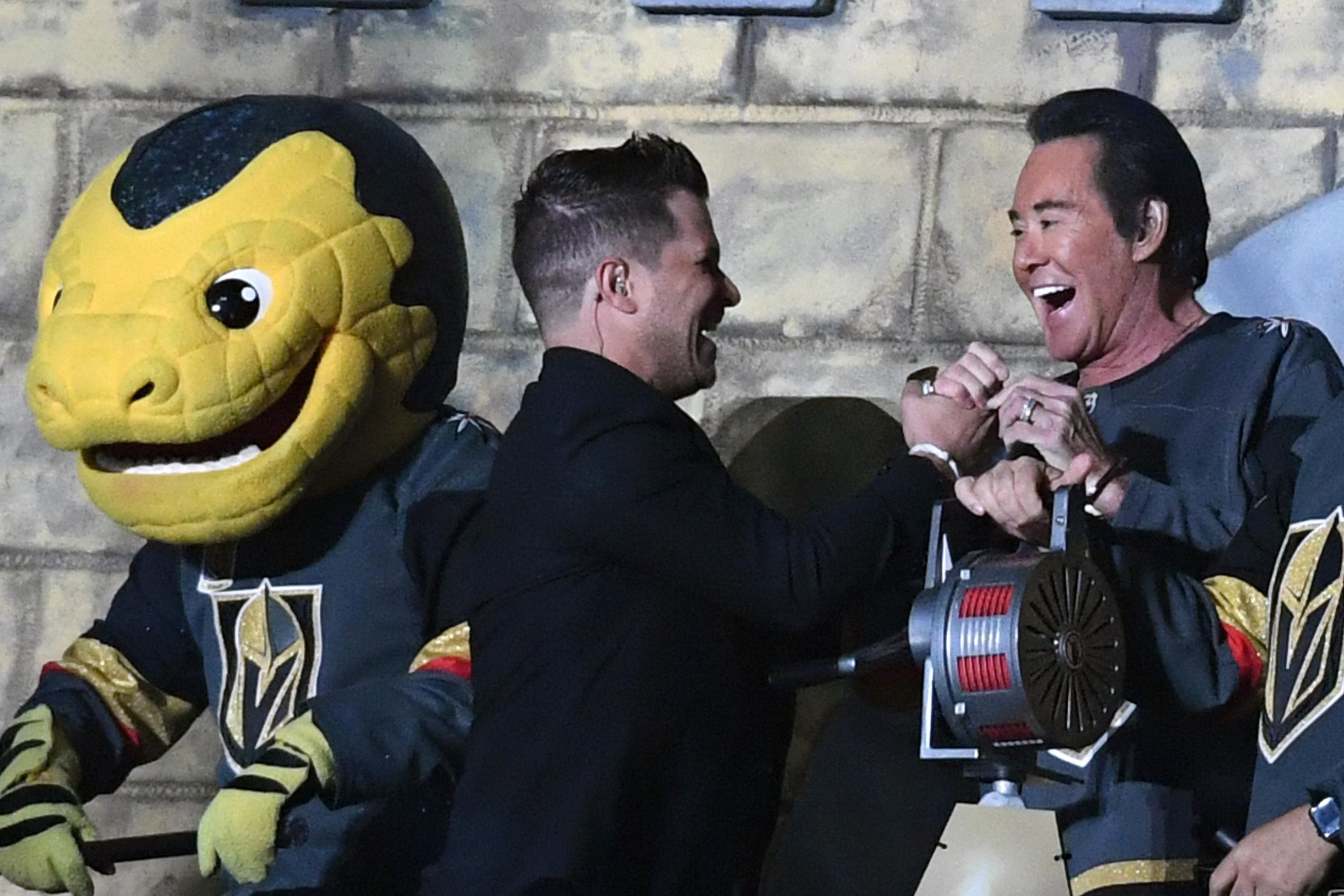 LAS VEGAS, NV - MAY 18:  The Vegas Golden Knights mascot Chance the Golden Gila Monster, Golden Knights host Mark Shunock and entertainer Wayne Newton react after Newton sounded a siren in the Castle before the start of the first period of Game Four of the Western Conference Finals between the Winnipeg Jets and the Golden Knights during the 2018 NHL Stanley Cup Playoffs at T-Mobile Arena on May 18, 2018 in Las Vegas, Nevada. The Golden Knights won 3-2.  (Photo by Ethan Miller/Getty Images)