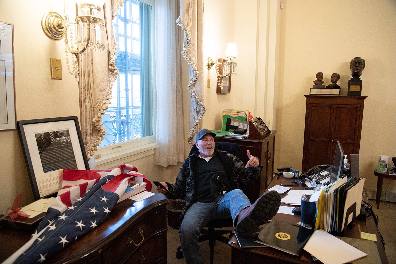 A man in a baseball cap sits with his left foot up on Speaker of the House Nancy Pelosi's desk.