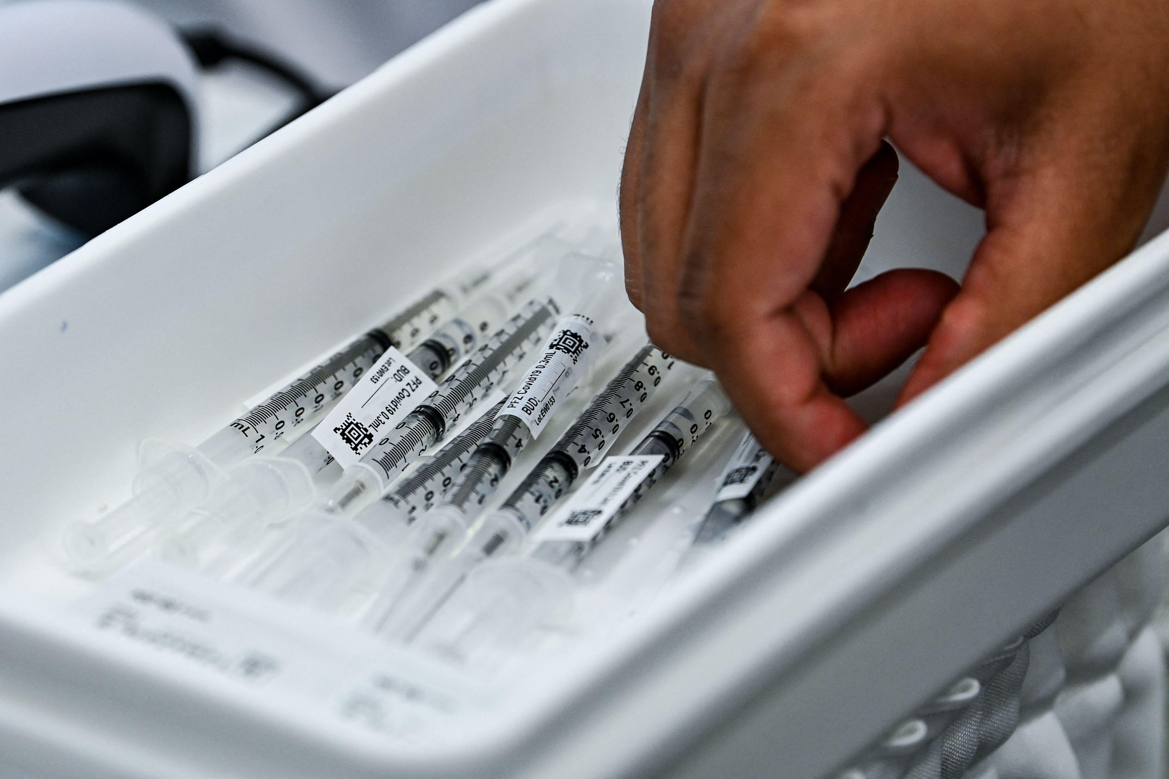 A hand reaches into a bin of vaccine syringes.