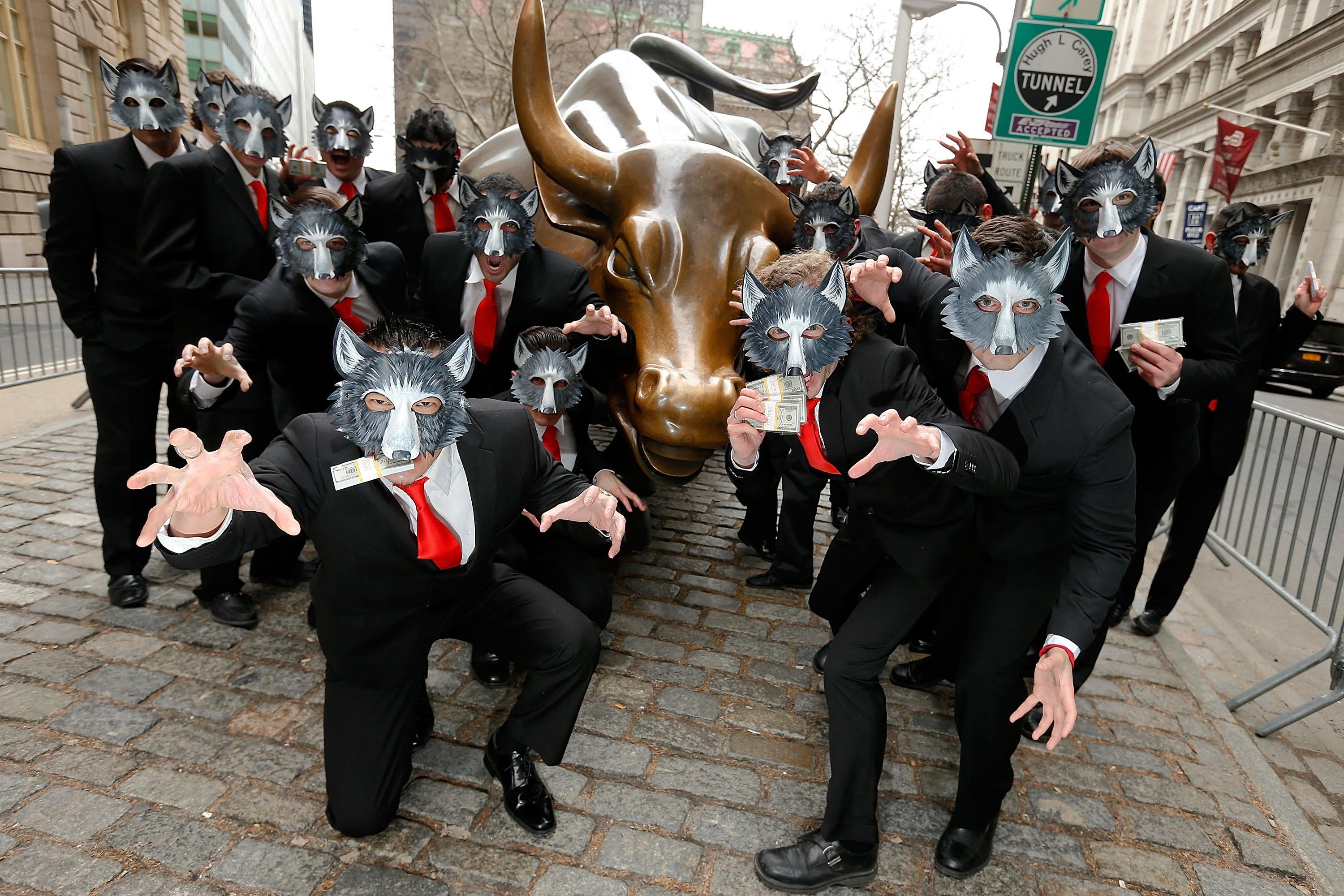 A bunch of people in wolf masks in front of the Wall Street bull statue.
