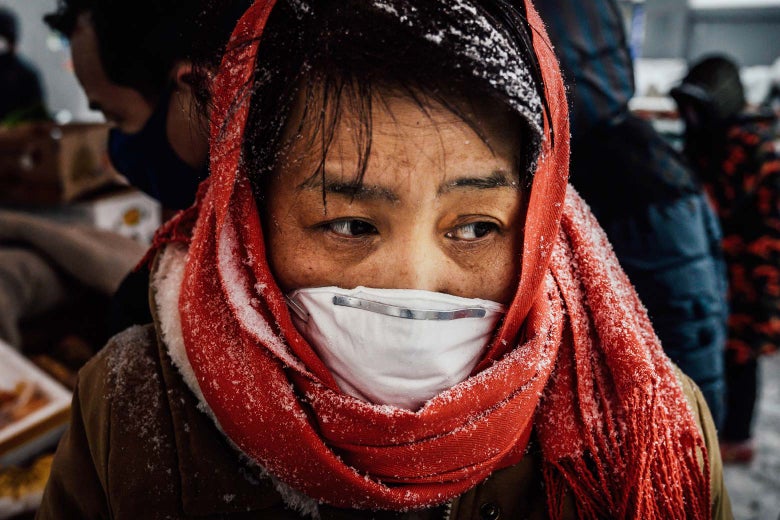 A woman with a red scarf wrapped around her head and wearing a surgical mask looks to the side.