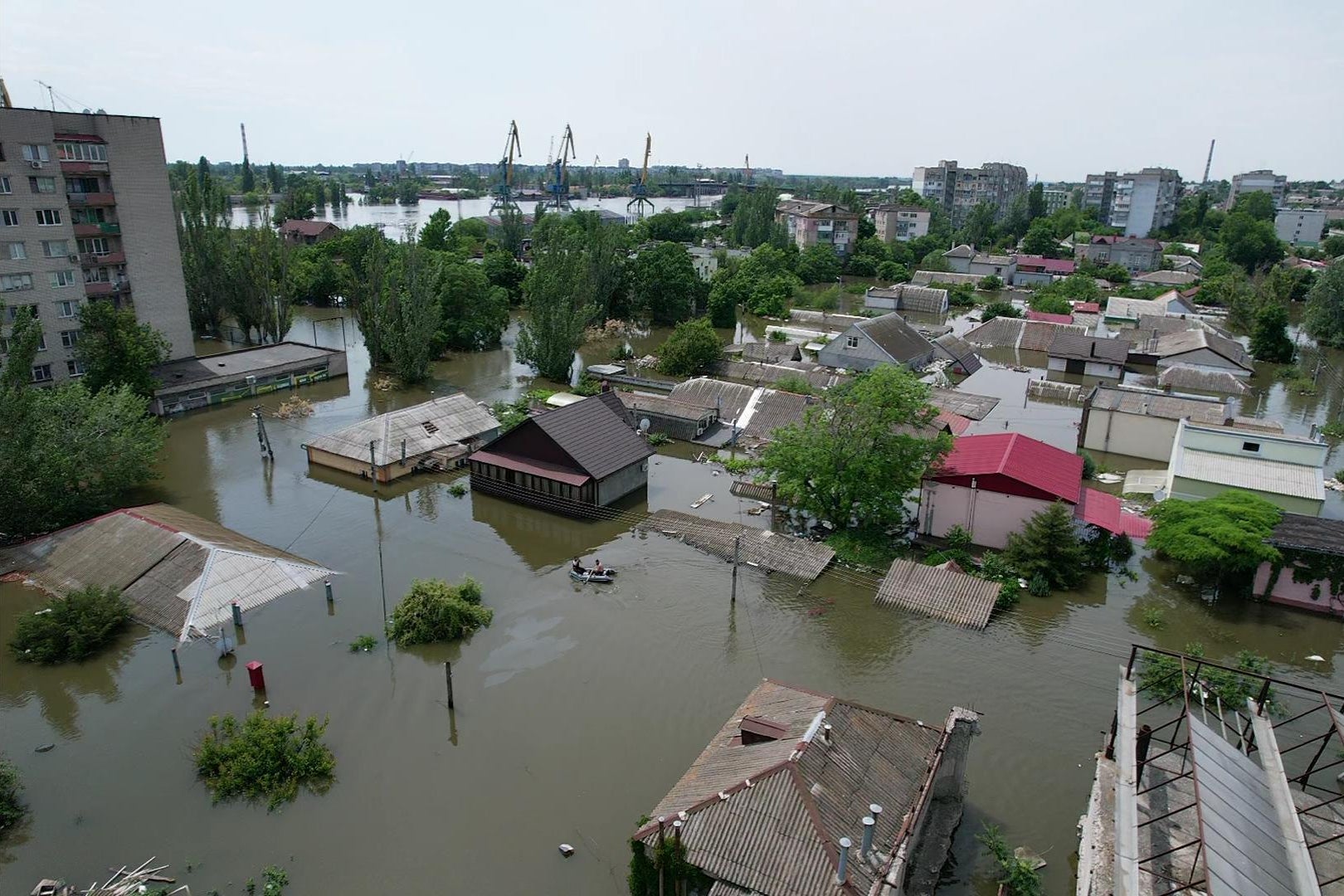 An overhead view of a flooded residential area, with two boaters floating between the buildings