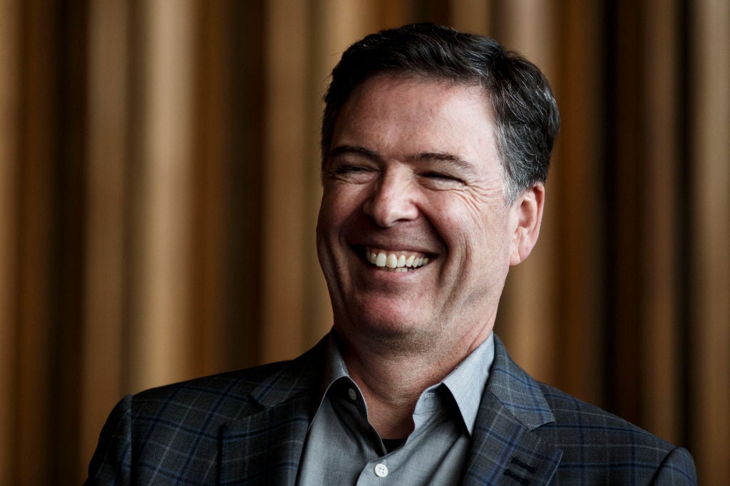 Comey, dressed in a sport coat against a backdrop of brown curtains, laughs.