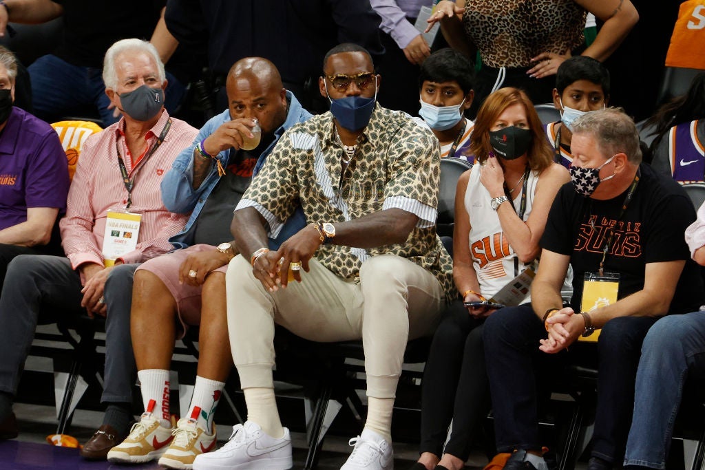 James, wearing a mask over his mouth but not his nose, looks toward the court from a front-row seat.