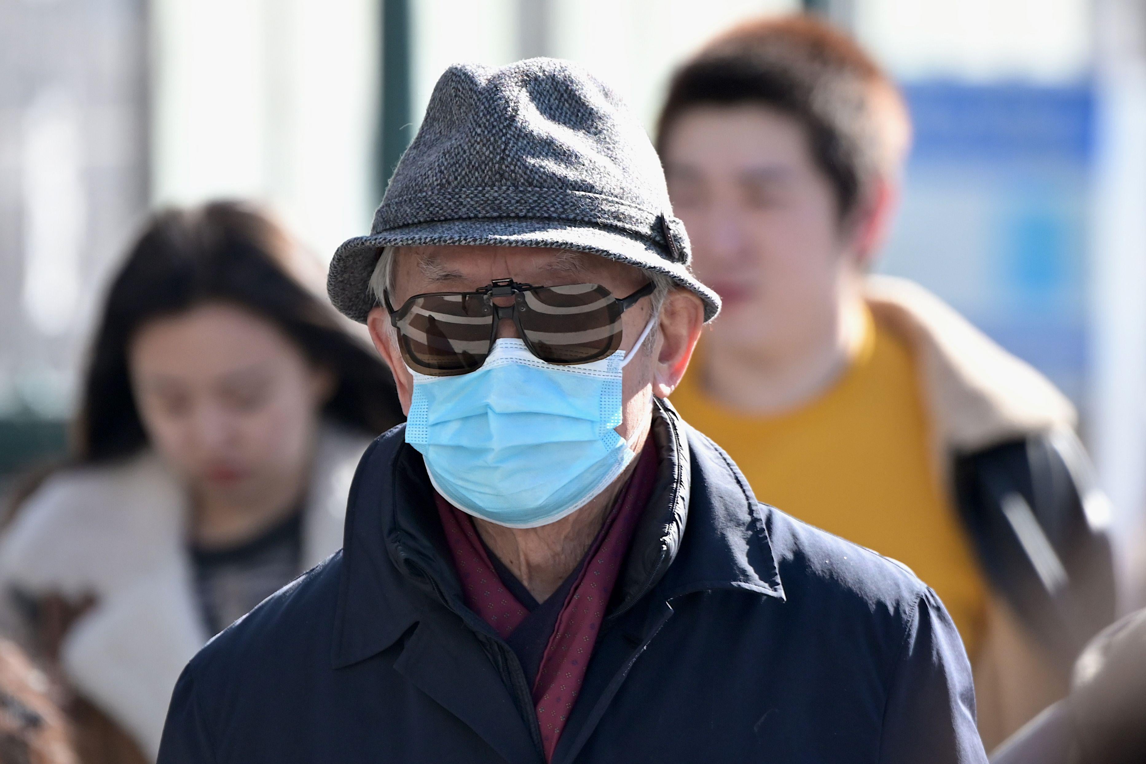 Man wearing a surgical mask and sunglasses, walking outside.