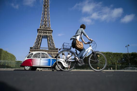 A cyclist rides past a French Citroen 2CV parked in front of the famous Eiffel Tower in Paris on August 3, 2012.
