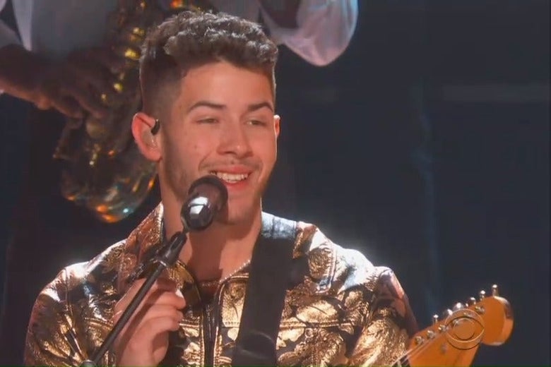 Nick Jonas performs at the Grammys, singing into the microphone and smiling, with a piece of food visibly stuck between his teeth.