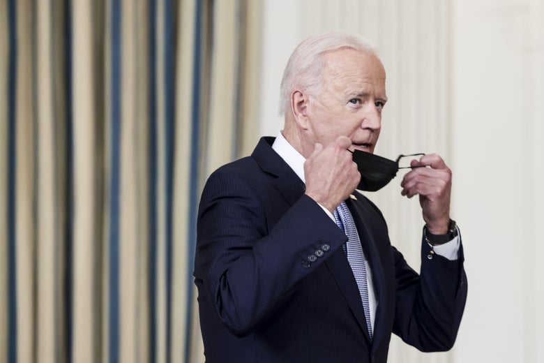 Biden, wearing a dark suit and blue tie, removing his mask as he arrives to deliver remarks.