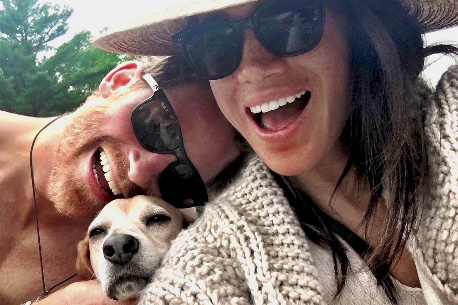 A man and woman both in sunglasses with their dog taking a selfie.
