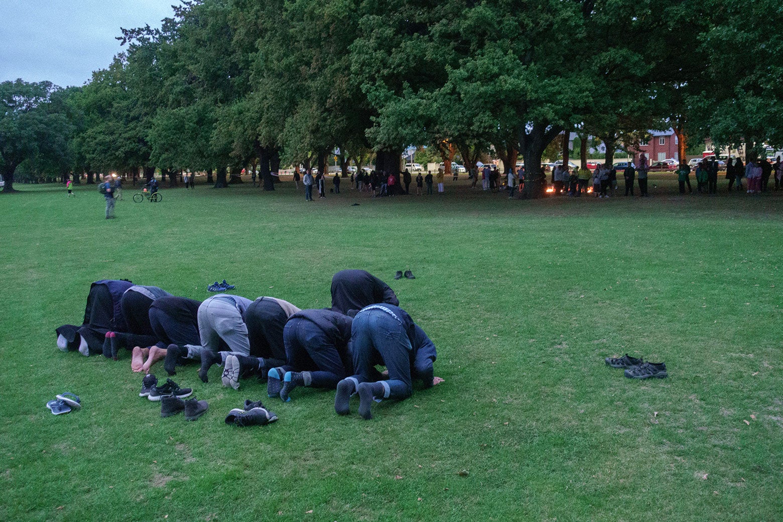 Eight men kneel to pray in a park.