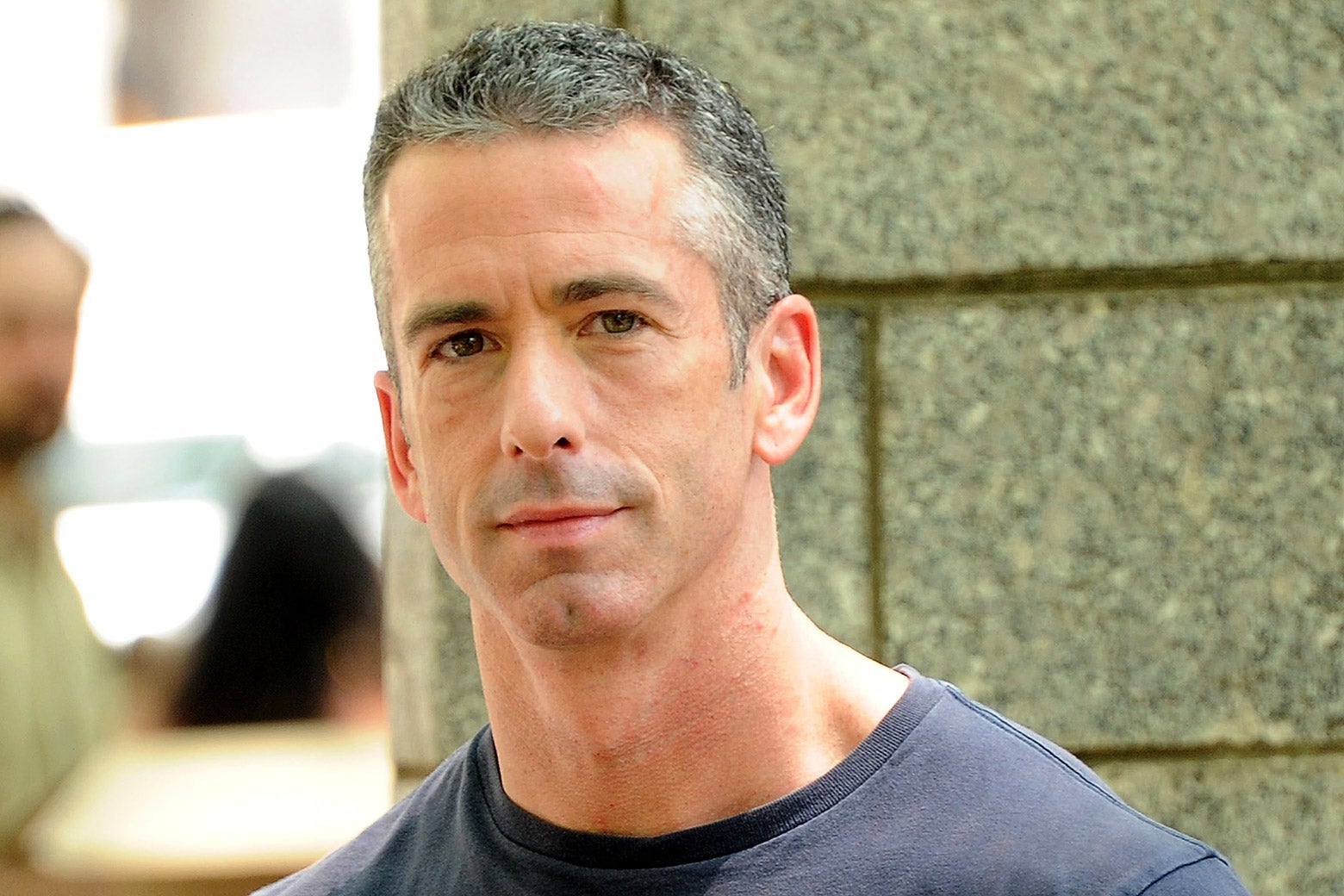 Dan Savage, outside against a cement wall.