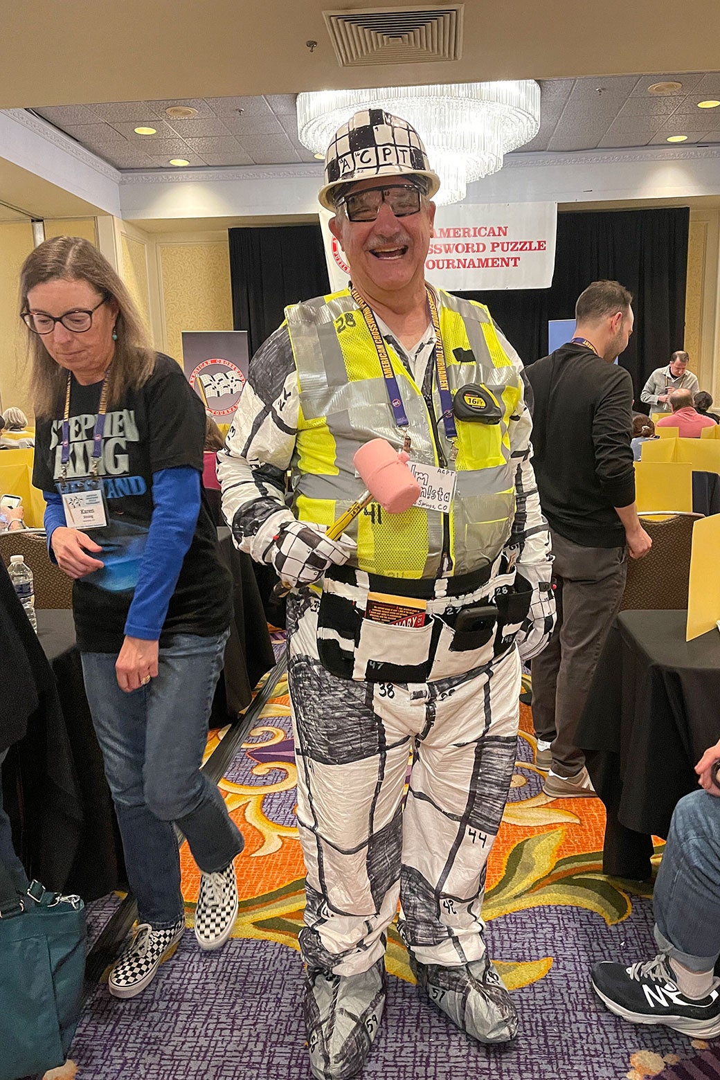 A man smiling and wearing a crossword-patterned outfit and hard hat.