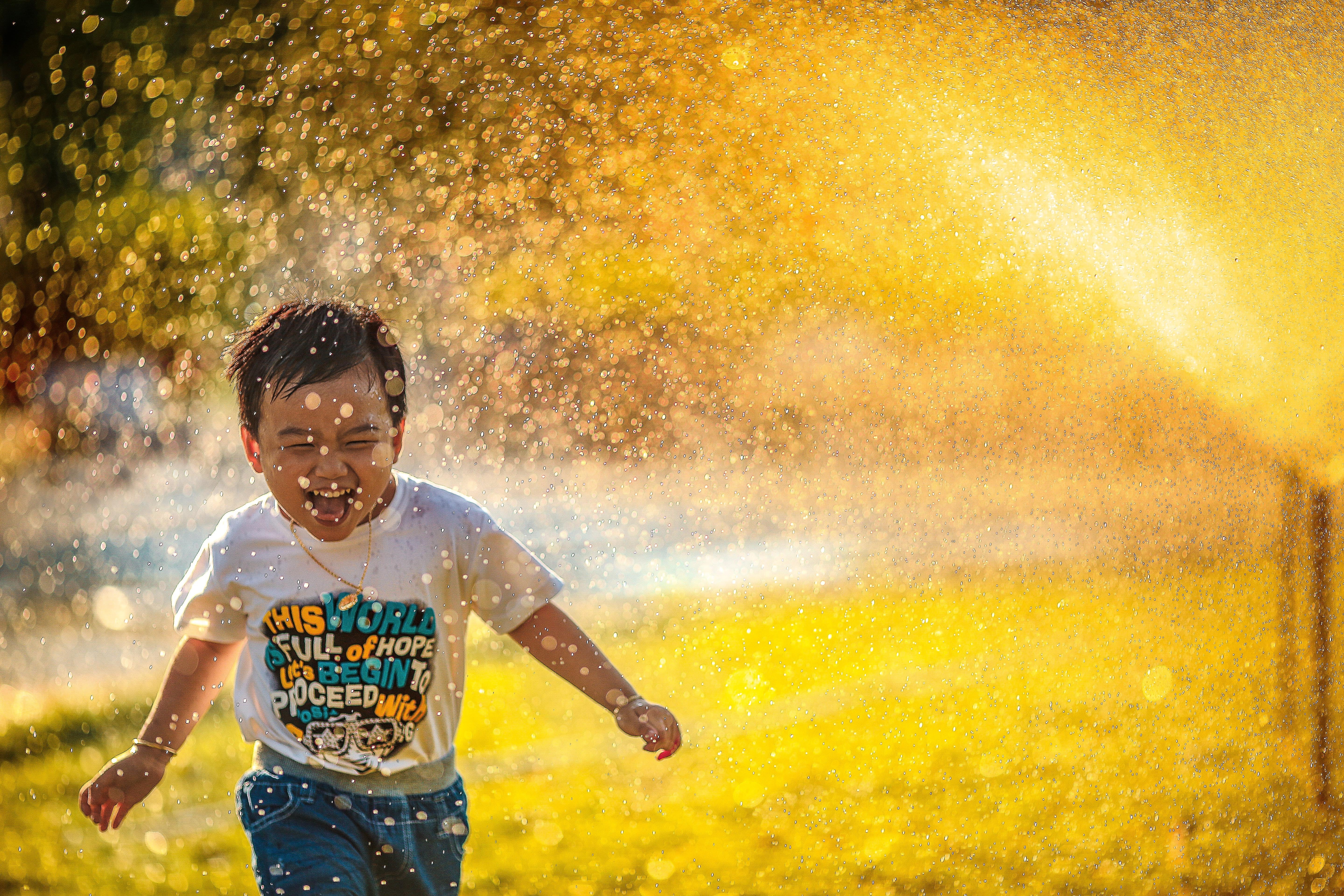 A young boy runs through a sprinkler.