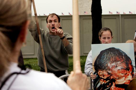 Pro Life Protester yelling alongside a graphic image of an aborted fetus.