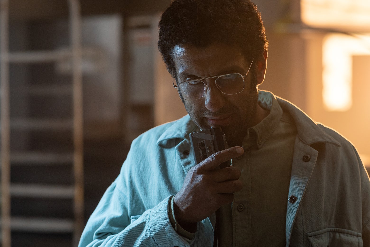 Actor Adeel Akhtar as Dr. Singh in a still from Sweet Tooth, wearing a denim shirt and speaking into a microcassete recorder.