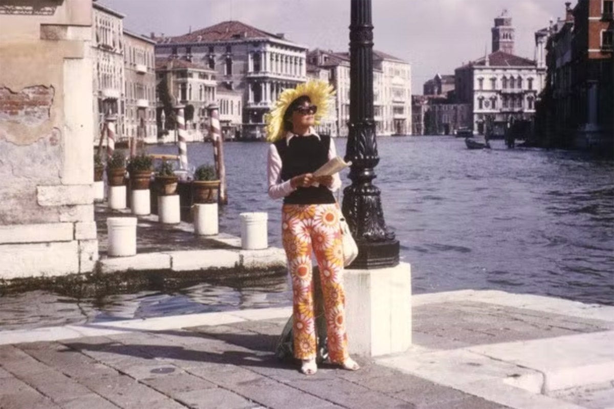 A woman with flowery pants stands by a canal in Venice.