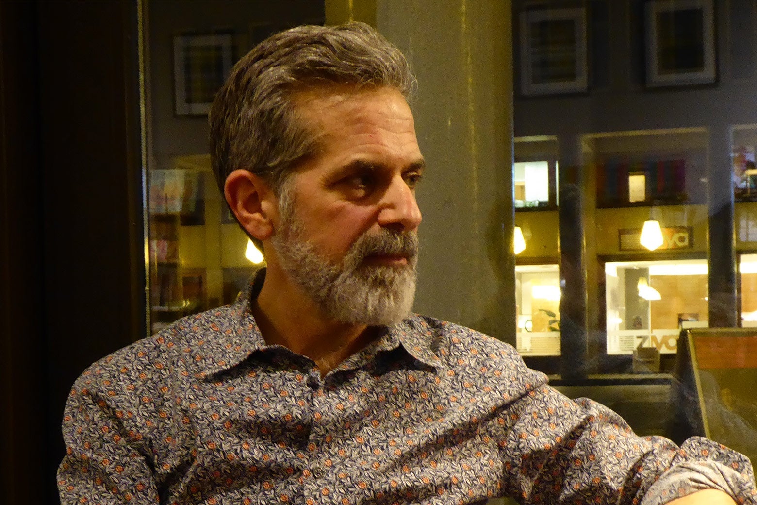 A middle aged white man with gray hair and a beard is wearing a flowery shirt.