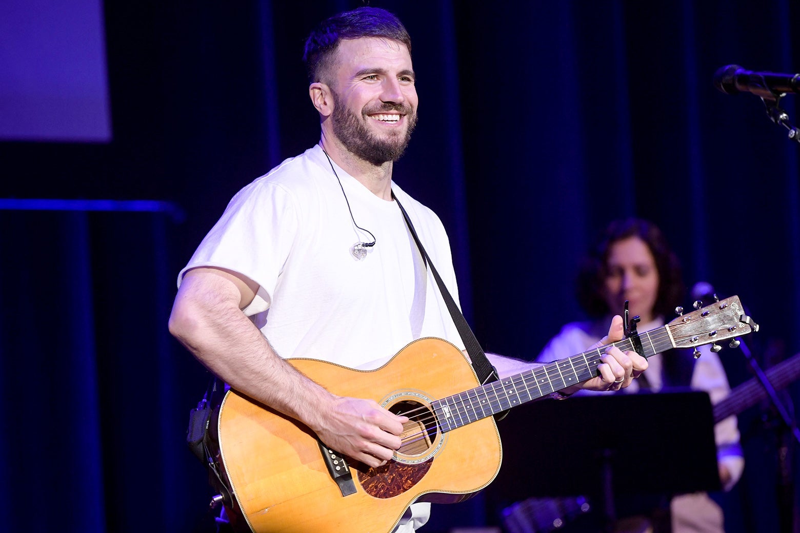 Sam Hunt in a white T-shirt holding an acoustic guitar.