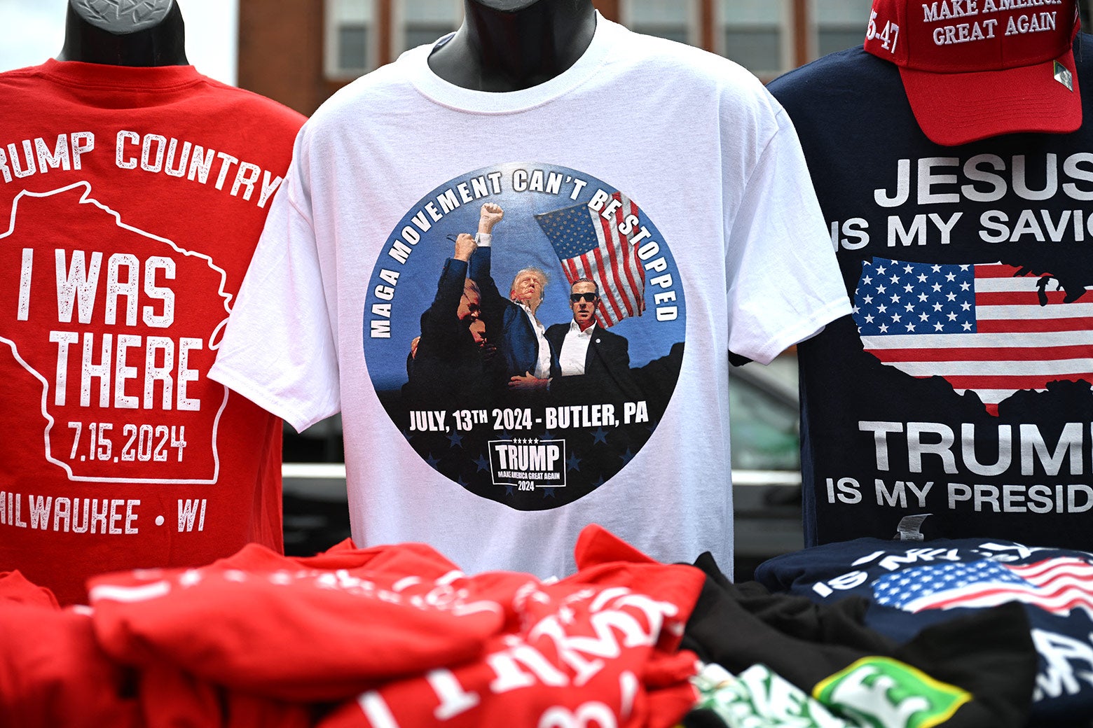 A white t-shirt depicts a photo of Donald Trump raising his fist moments after his ear was grazed by a bullet during a campaign rally in Butler, Pennsylvania, with the phrase 