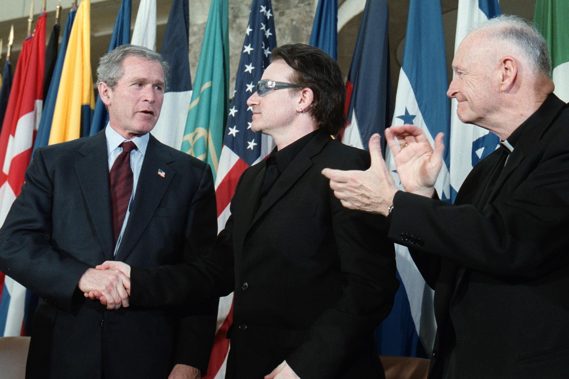 George W. Bush shaking hands with Bono, as Theodore McCarrick looks on, applauding.