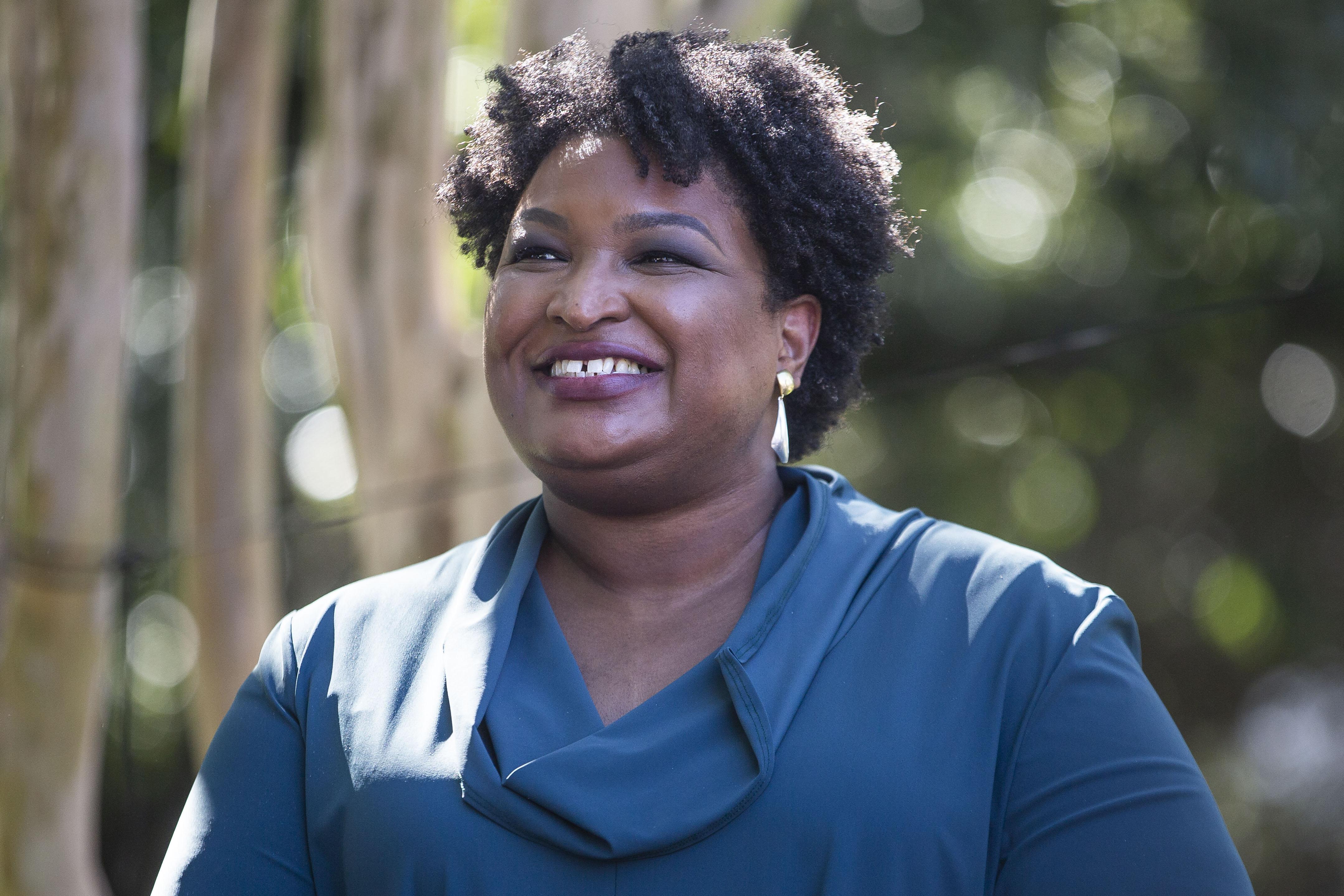 Stacey Abrams in a cowl neck shirt smiling outside