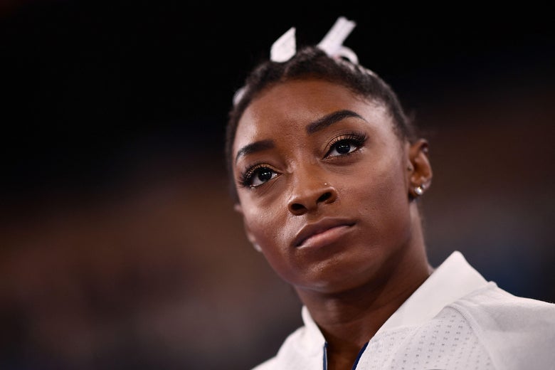 Simone Biles looking serious as she stands on the sidelines