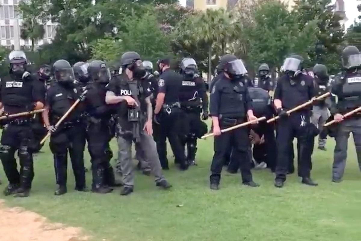 A line of police officers is seen in a video; the officers in the center are leading Jordan away, though he is obscured by their backs.