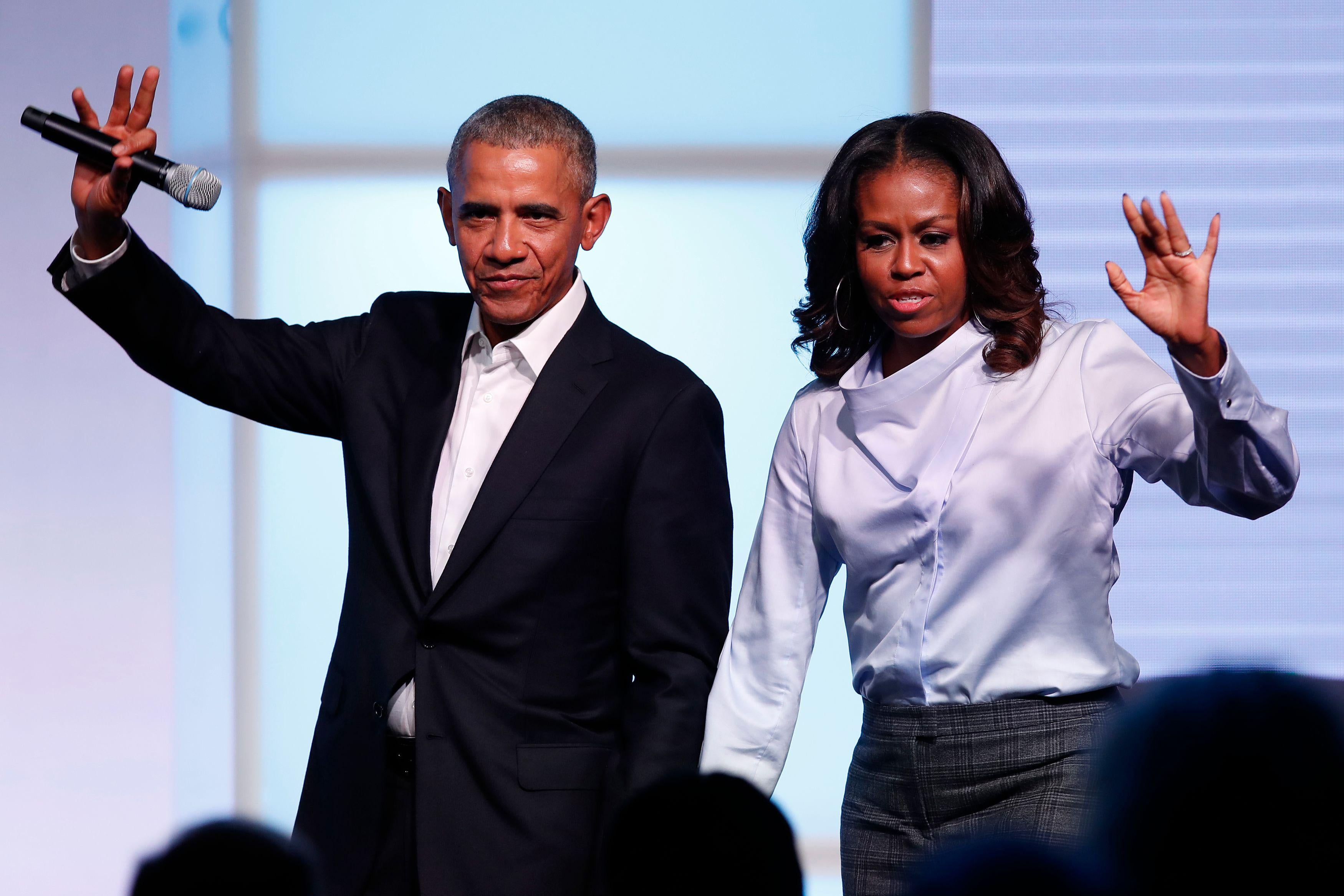 Barack and Michelle Obama hold hands on stage and wave out at the crowd.