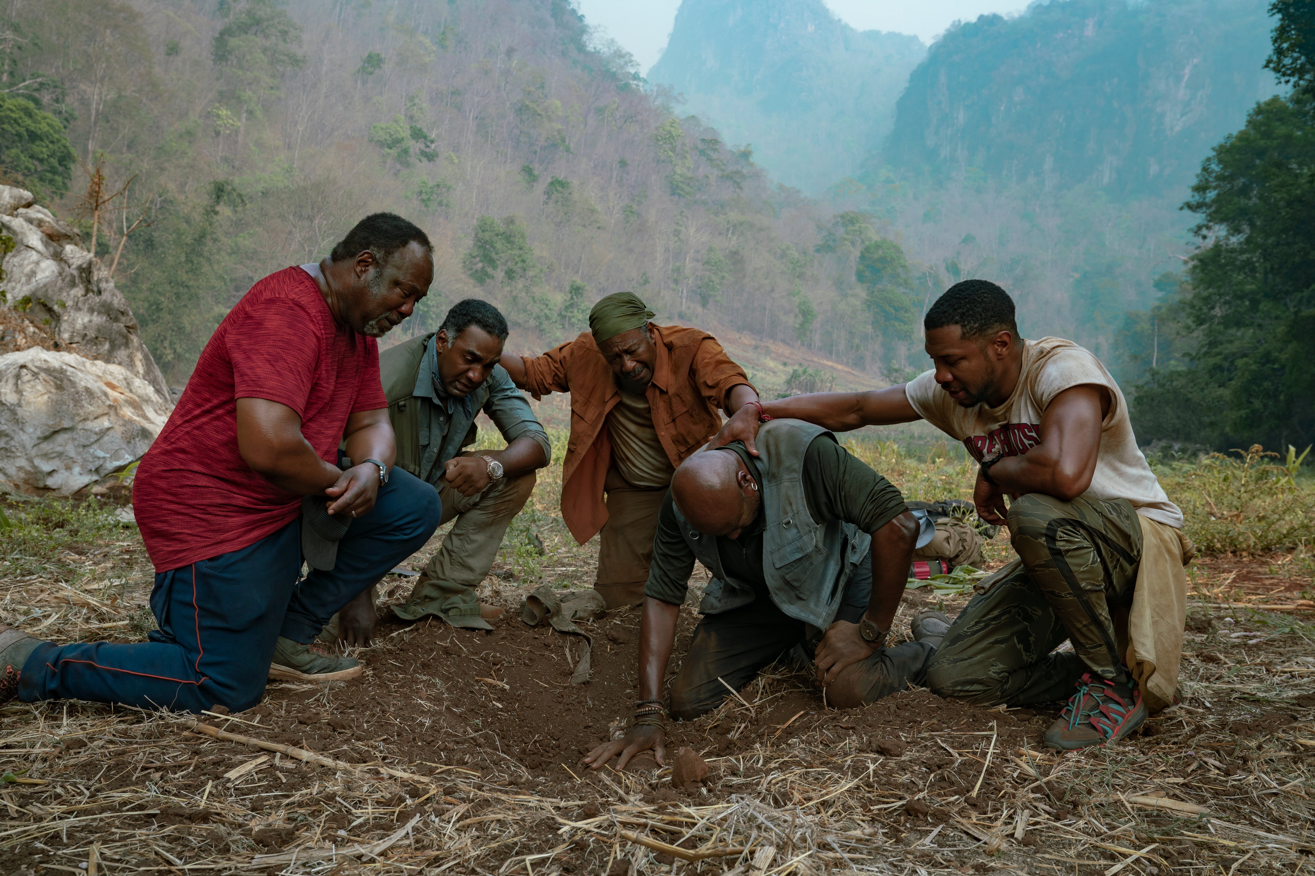 Still from Da 5 Bloods shows actors Delroy Lindo, Clarke Peters, Isiah Whitlock Jr., Norm Lewis, and Jonathan Majors kneeling solemnly around a hole in the ground.