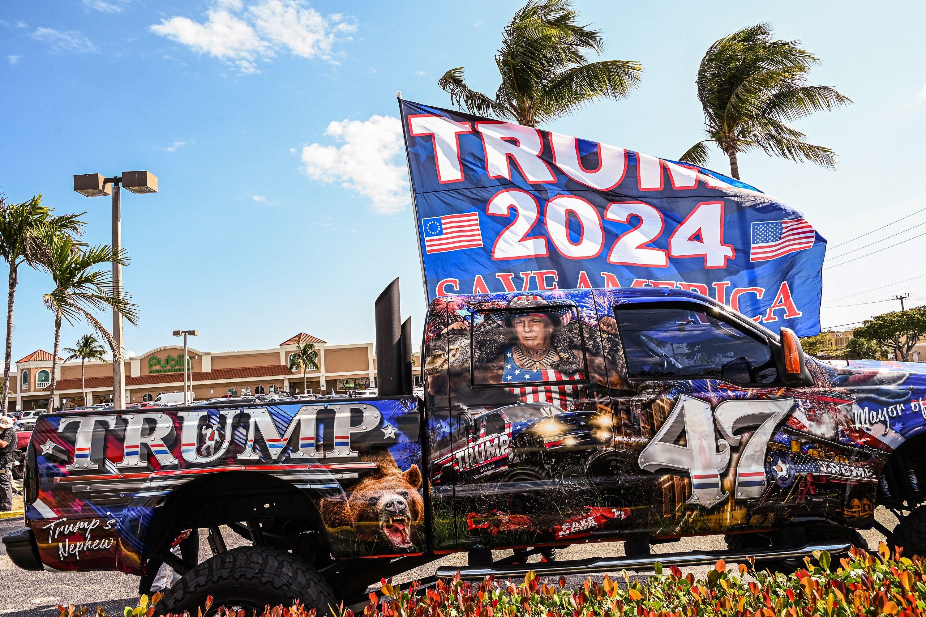 Trump 2024 Save America banner hangs in front of a decked out Trump painted truck.