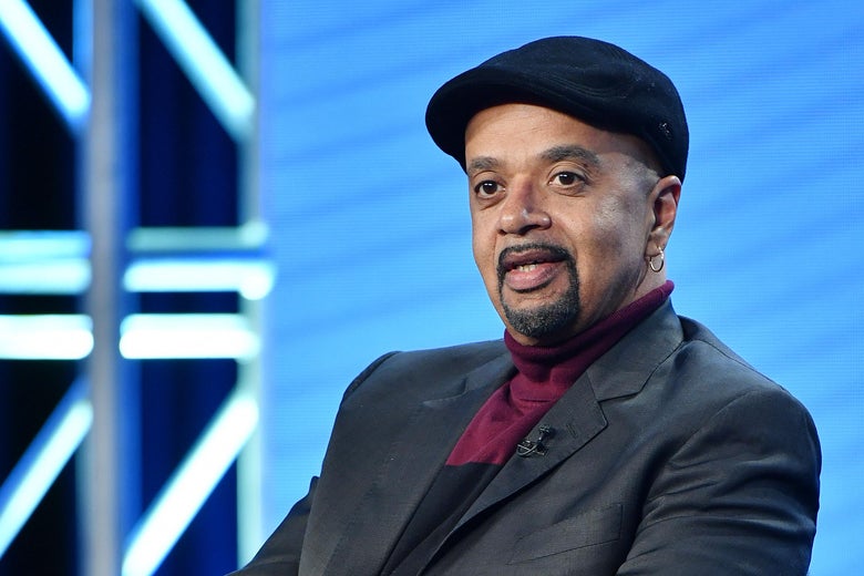 A man wearing a jaunty cap sits on a stage.