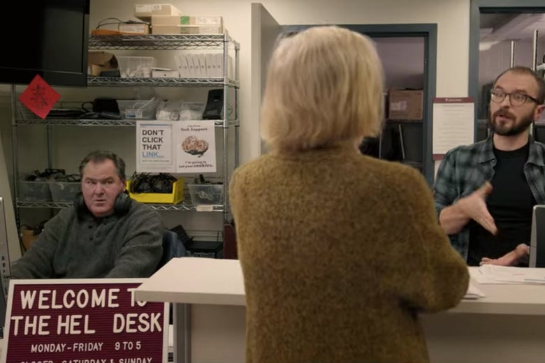 Joan standing at an IT desk talking to two men.