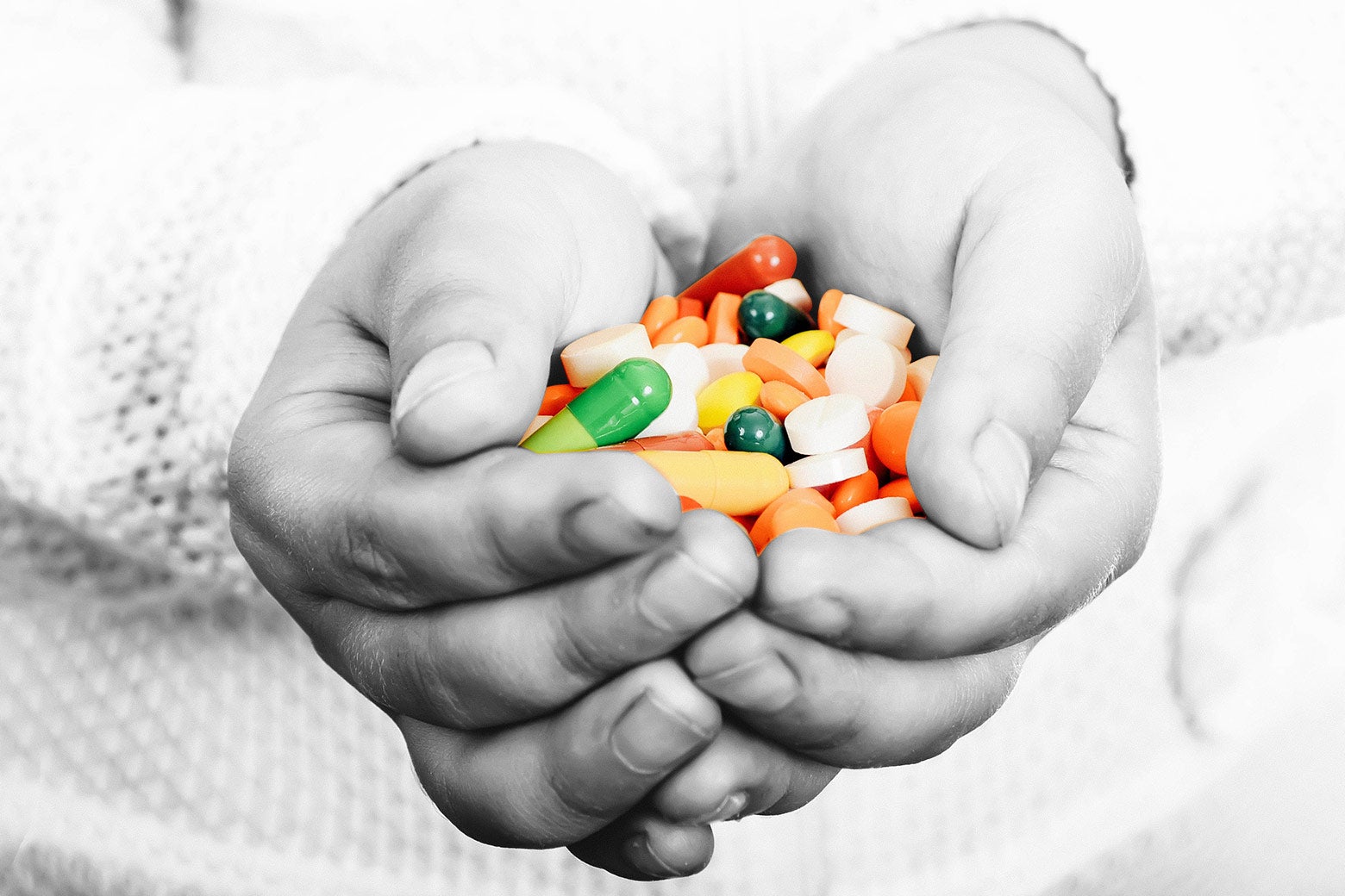 A child's hands cupping a colorful assortment of prescription pills.