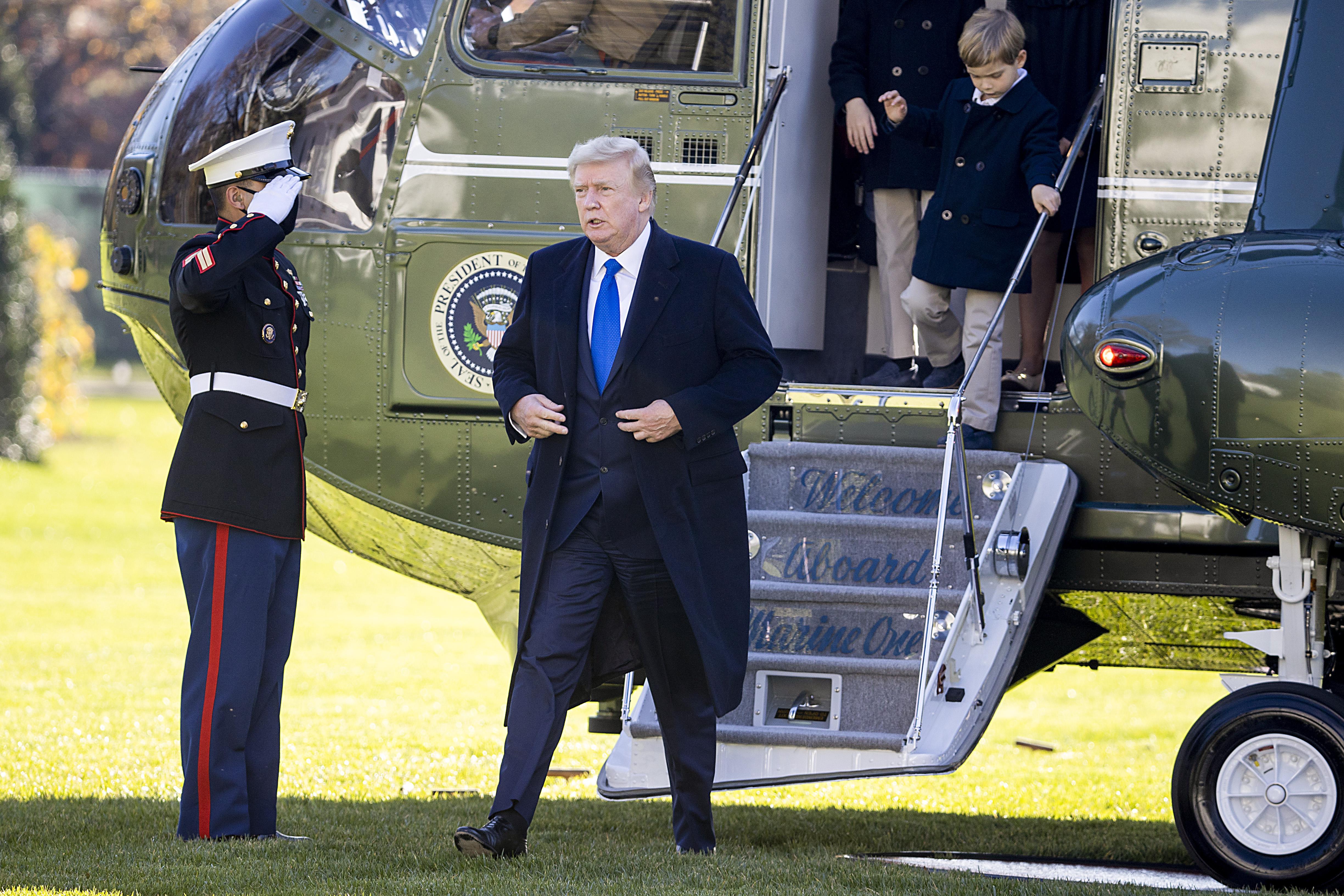 Trump walks away from Marine One on the South Lawn of the White House, past a uniformed service member saluting him.
