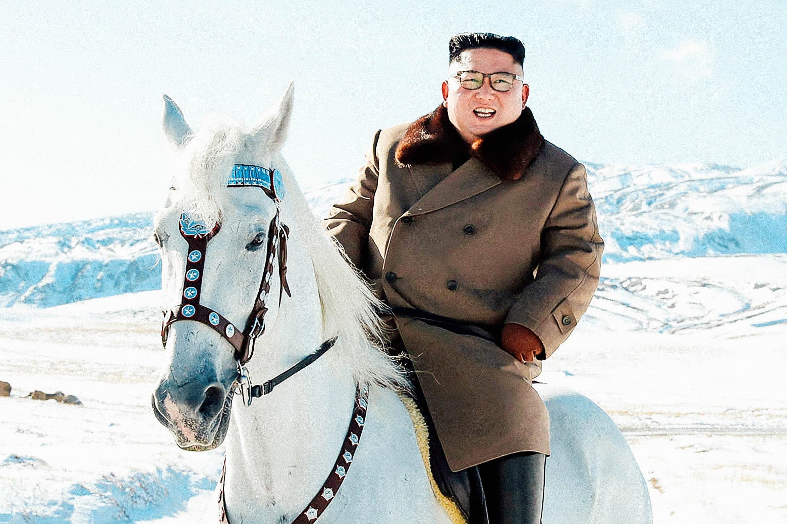 Kim grinning, astride a white horse, with snow-capped mountains in the background.