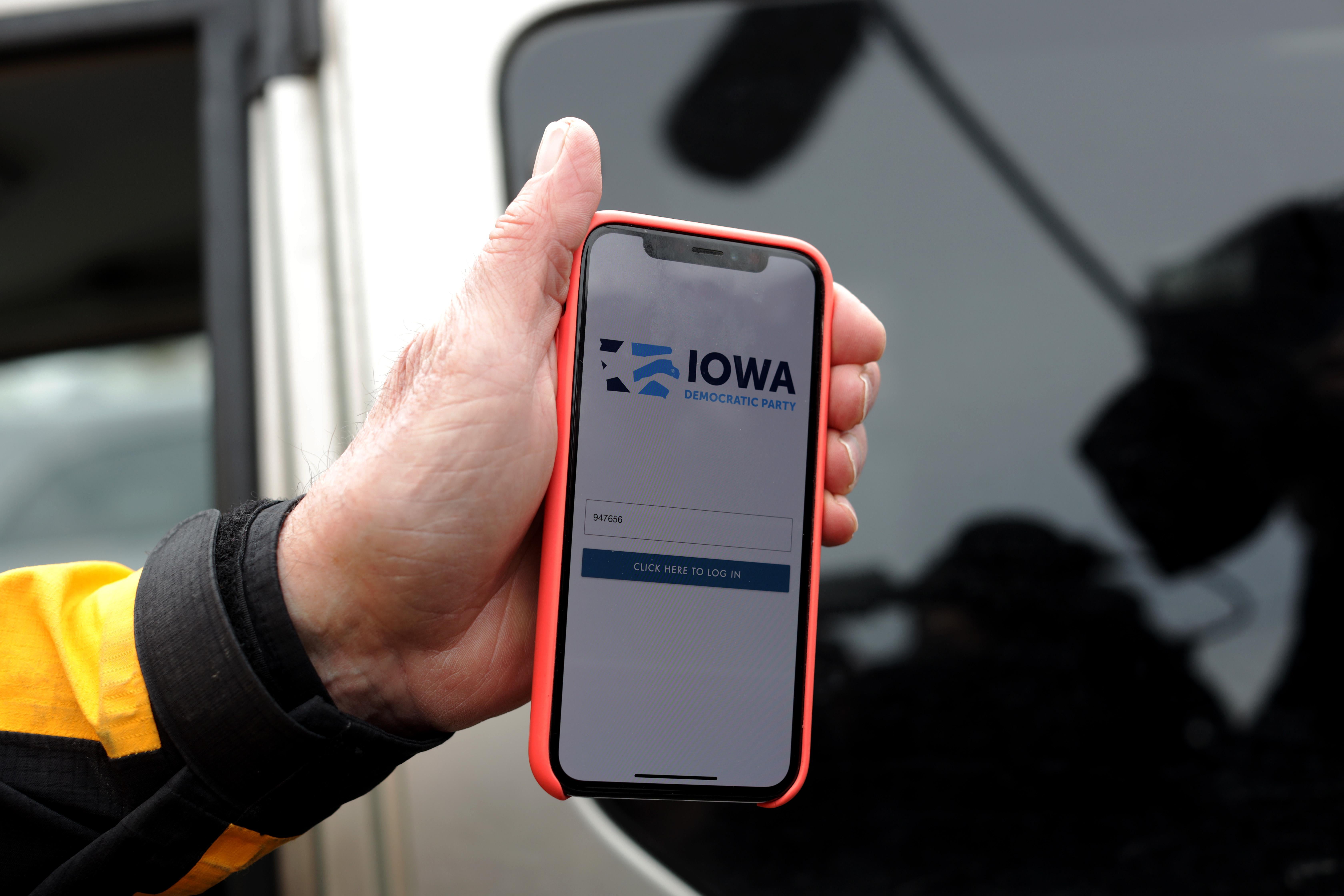 A hand holds a smartphone showing the sign-in interface for the Iowa vote reporting app.
