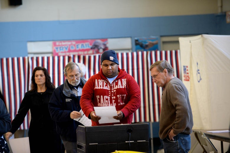 A line of voters wait to submit their ballots to a scanner. 