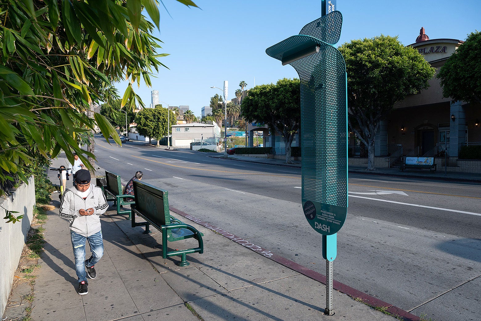 A little metal shade is connected to a pole near a bus stop.