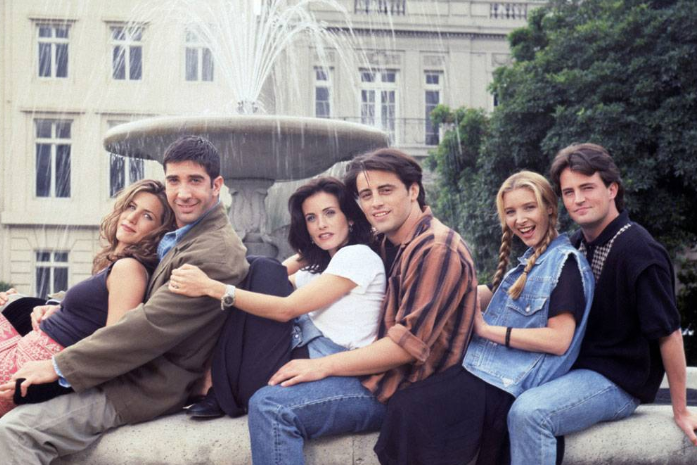 The Friends cast sits on a water fountain.